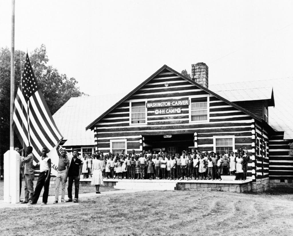 Historic black and white photo of children posing in front of a 4-H camp lodge